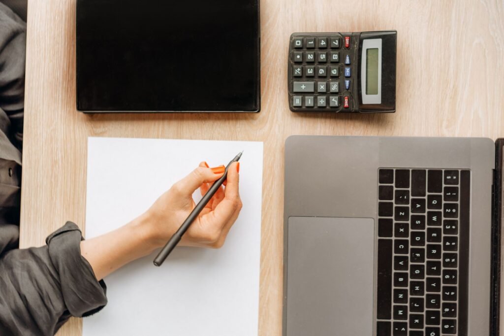 Dental practice owner calculating costs and revenue on a calculator and laptop