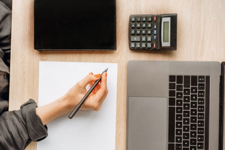 Dental practice owner calculating costs and revenue on a calculator and laptop